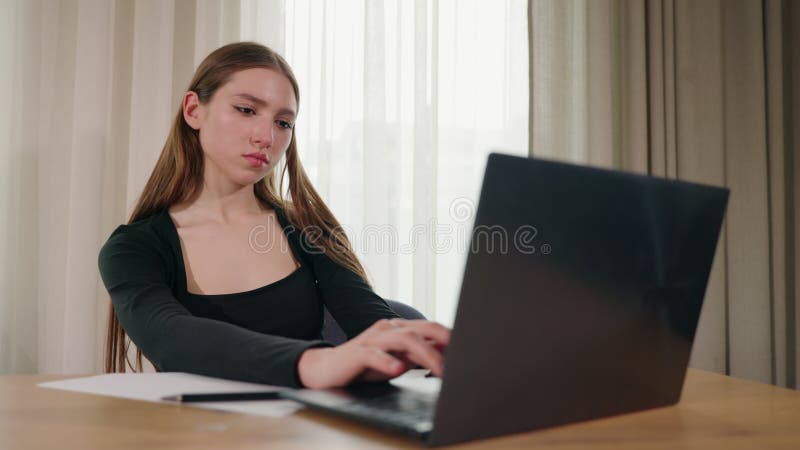 Giovane donna concentrata che scrive sul computer portatile all'ufficio centrale vicino alla finestra stock footage