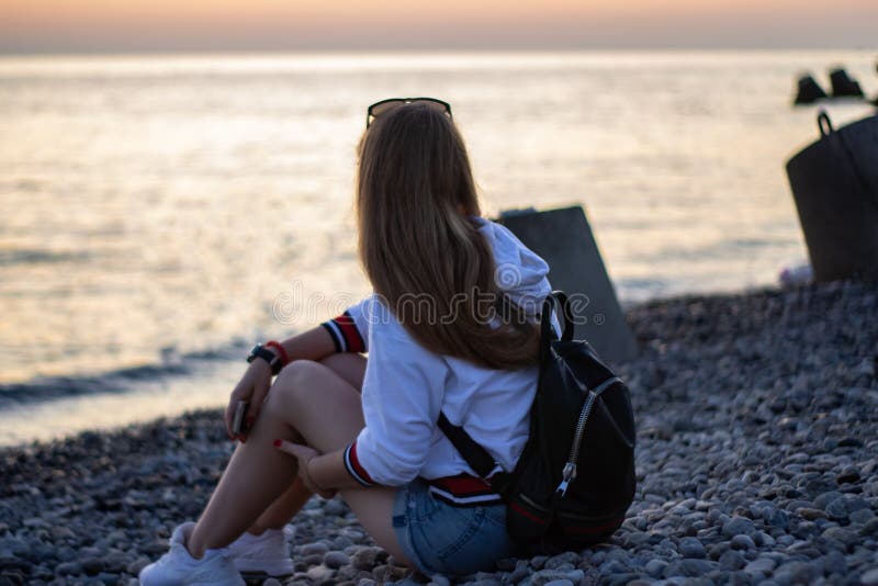 Giovane donna dai capelli rossi seduta sulle rocce e a guardare il tramonto sul mare immagini stock Giovane donna dai capelli rossi seduta sulle rocce e a guardare il tramonto sul mare immagini stock