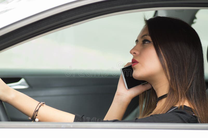Giovane donna del primo piano che si siede nella tenuta dell'automobile che parla sulla tazza di caffè e del telefono cellulare, immagine stock libera da diritti Giovane donna del primo piano che si siede nella tenuta dell'automobile che parla sulla tazza di caffè e del telefono cellulare, immagine stock libera da diritti