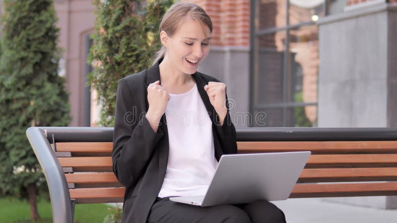 Giovane donna di affari Celebrating sul computer portatile che si siede fuori dell'ufficio