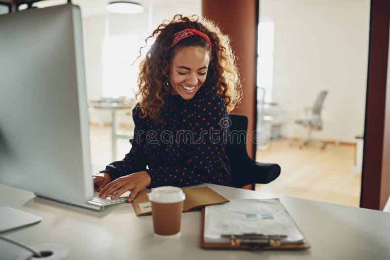 Giovane donna di affari che sorride mentre lavorando alla sua scrivania fotografia stock Giovane donna di affari che sorride mentre lavorando alla sua scrivania fotografia stock