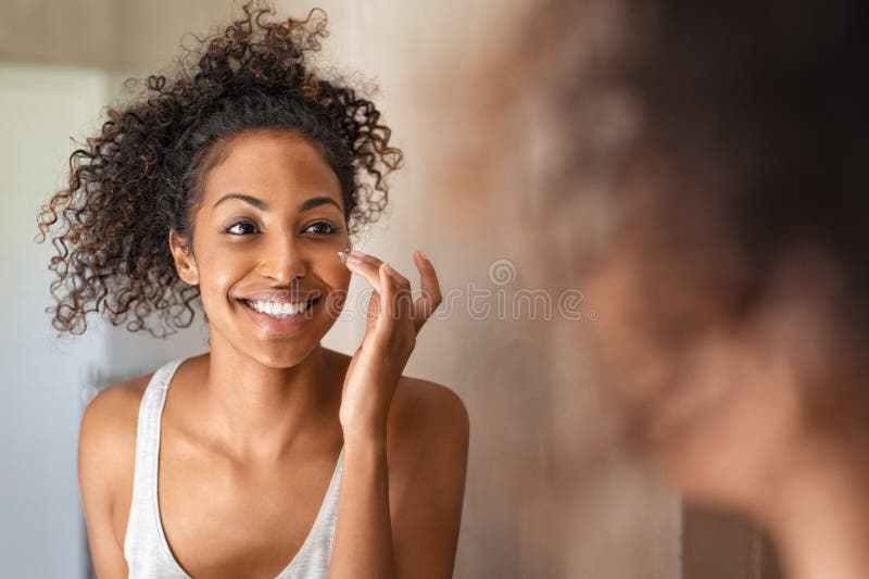 Giovane donna di colore che applica la crema per la pelle