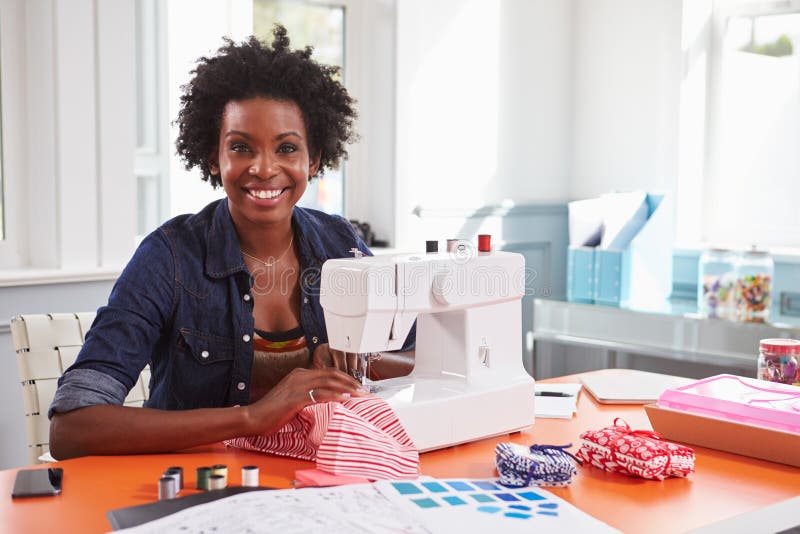 Giovane donna di colore che usando una macchina per cucire che guarda alla macchina fotografica