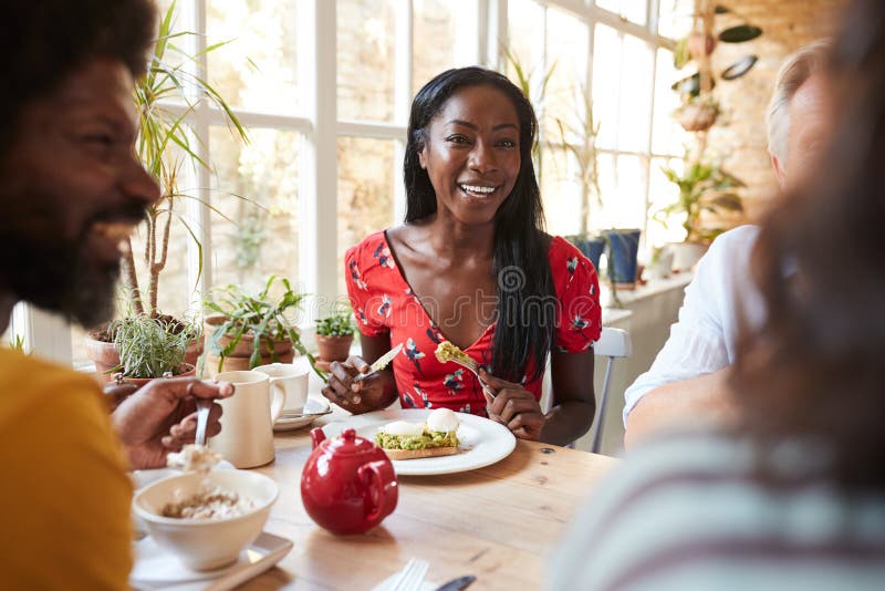 Giovane donna di colore felice che mangia brunch con gli amici ad un caffè
