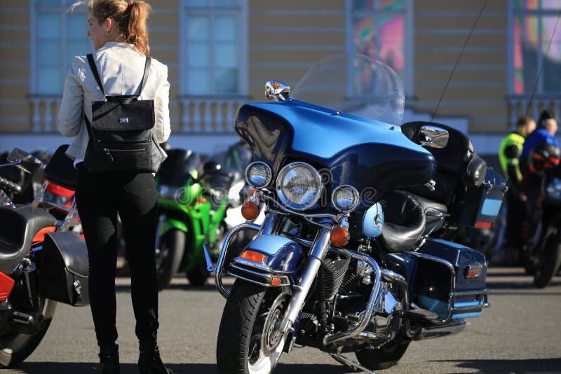 Giovane donna e motociclo blu parcheggiato di Harley-Davidson un giorno soleggiato immagini stock Giovane donna e motociclo blu parcheggiato di Harley-Davidson un giorno soleggiato immagini stock