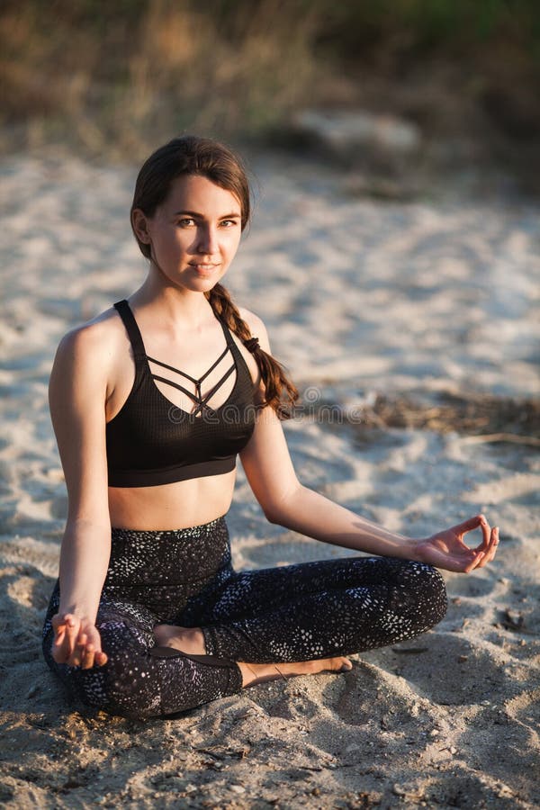 Giovane donna esile di sorriso felice in Lotus Position che esamina macchina fotografica la spiaggia di sabbia Copi lo spazio Spo fotografie stock libere da diritti Giovane donna esile di sorriso felice in Lotus Position che esamina macchina fotografica la spiaggia di sabbia Copi lo spazio Spo fotografie stock libere da diritti