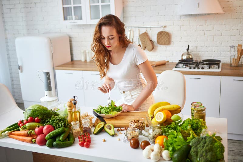 Giovane donna felice che mangia insalata nella bella cucina con gli ingredienti freschi verdi all'interno Concetto sano dell'alim fotografie stock