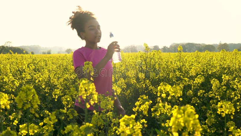 Giovane donna femminile dell'adolescente afroamericano della ragazza che beve dalla bottiglia di acqua e che corre o che pareggia