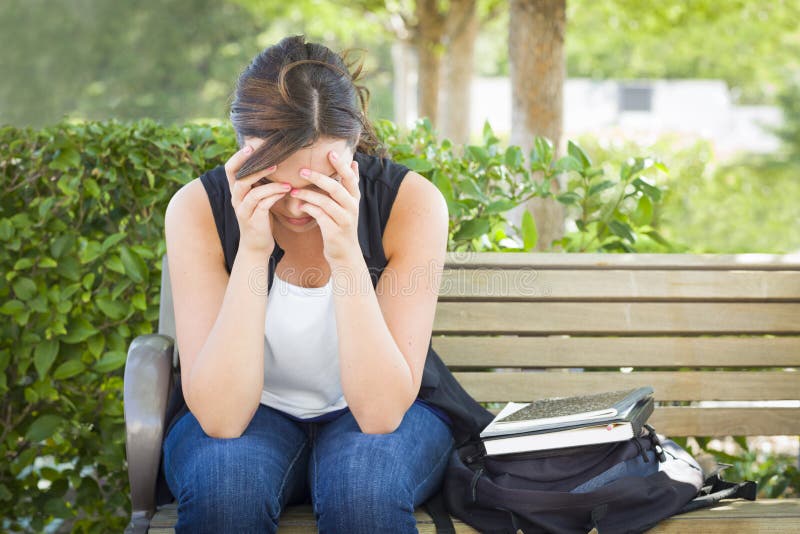 Giovane donna frustrata che si siede da solo sul banco accanto ai libri immagine stock Giovane donna frustrata che si siede da solo sul banco accanto ai libri immagine stock