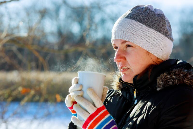 Giovane donna graziosa che beve tè caldo un giorno di inverno freddo immagine stock Giovane donna graziosa che beve tè caldo un giorno di inverno freddo immagine stock