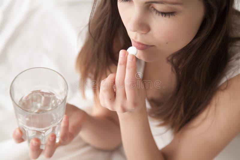 Giovane donna malata non sana che prende il sonnifero in pillole che si siede a letto fotografie stock libere da diritti Giovane donna malata non sana che prende il sonnifero in pillole che si siede a letto fotografie stock libere da diritti