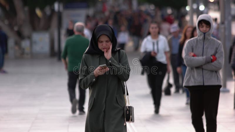 Giovane donna musulmana con il velo nero che usa il cellulare all'aperto.