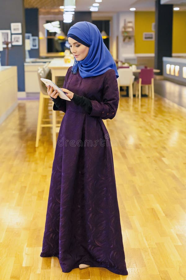 Giovane donna musulmana con una compressa elettronica in sue mani fotografia stock libera da diritti Giovane donna musulmana con una compressa elettronica in sue mani fotografia stock libera da diritti