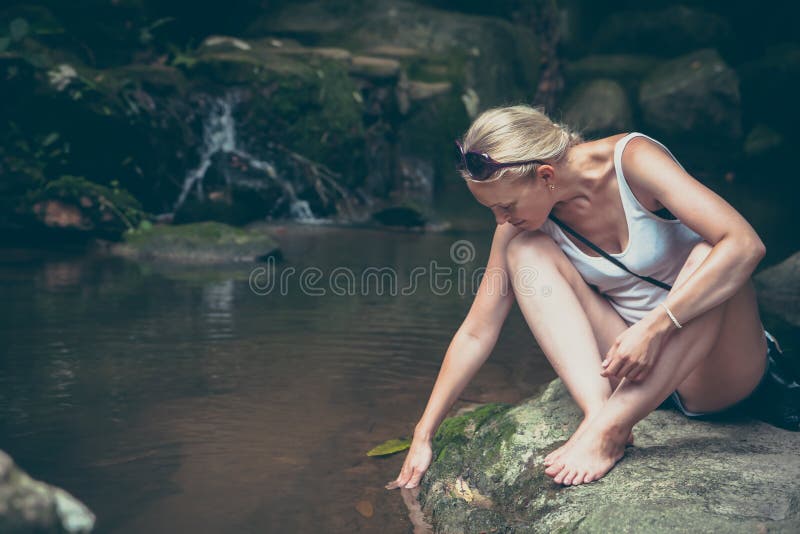 Giovane donna pensierosa che si rilassa il fiume vicino della montagna dopo l'escursione nello stile d'annata retro immagini stock libere da diritti Giovane donna pensierosa che si rilassa il fiume vicino della montagna dopo l'escursione nello stile d'annata retro immagini stock libere da diritti