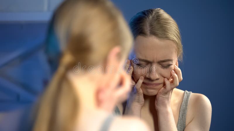 Giovane donna profondamente turbata che guarda tristemente specchio, insoddisfatto dell'aspetto, pubertà fotografia stock Giovane donna profondamente turbata che guarda tristemente specchio, insoddisfatto dell'aspetto, pubertà fotografia stock