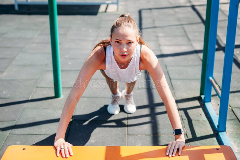 Giovane donna sexy sportiva che fa spinta-UPS dal banco sul campo sportivo Stile di vita sano di concetto fotografia stock libera da diritti Giovane donna sexy sportiva che fa spinta-UPS dal banco sul campo sportivo Stile di vita sano di concetto fotografia stock libera da diritti