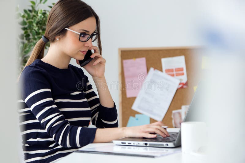 Giovane donna sicura che lavora nel suo ufficio con il computer portatile fotografia stock Giovane donna sicura che lavora nel suo ufficio con il computer portatile fotografia stock