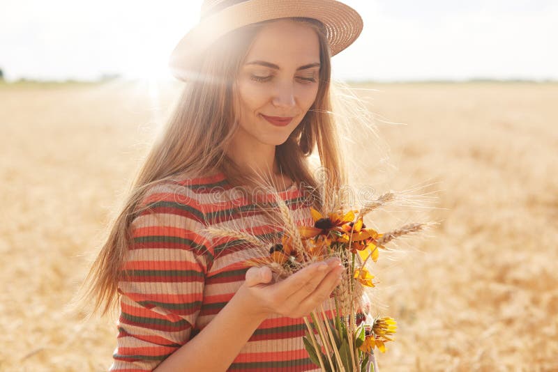 Giovane donna soddisfatta positiva che porta il cappello spogliato di paglia e del vestito, posante nel giacimento di grano, mazz fotografie stock libere da diritti