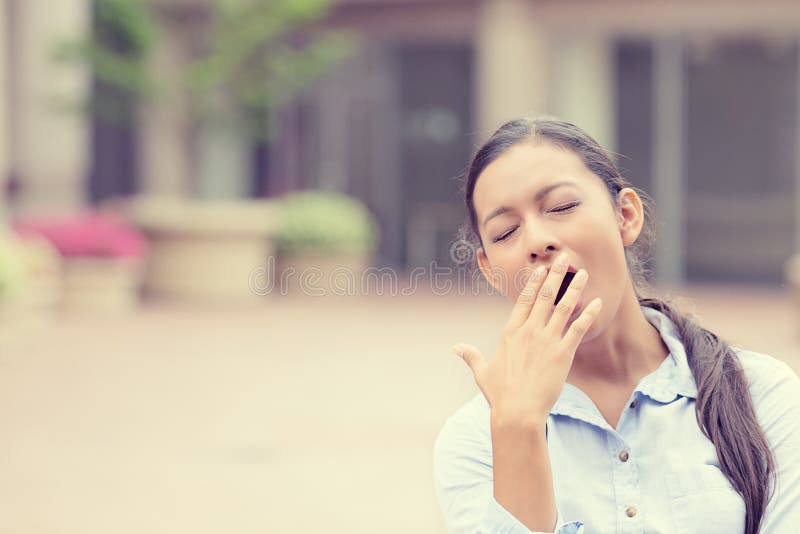 It is too early for this meeting. Portrait sleepy young business woman covering with hand wide open mouth yawning eyes closed looking bored isolated outside office background. Emotion face expression. It is too early for this meeting. Portrait sleepy young business woman covering with hand wide open mouth yawning eyes closed looking bored isolated outside office background. Emotion face expression