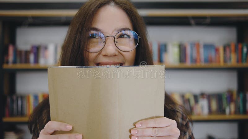 Giovane donna sorride intensamente mentre tiene in mano un libro in una comoda biblioteca durante una visita diurna stock footage