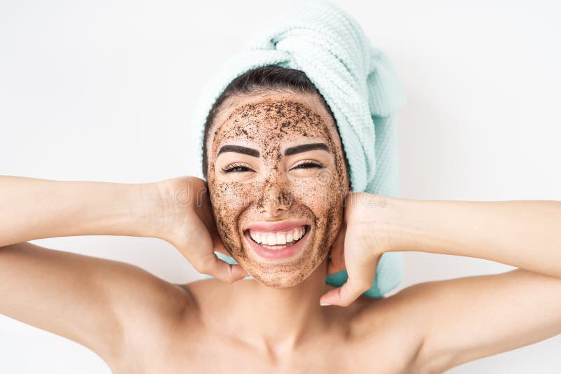 Giovane donna sorridente che applica una maschera per strofinacci di caffè sulla faccia felice ragazza che si occupa di pelle il g