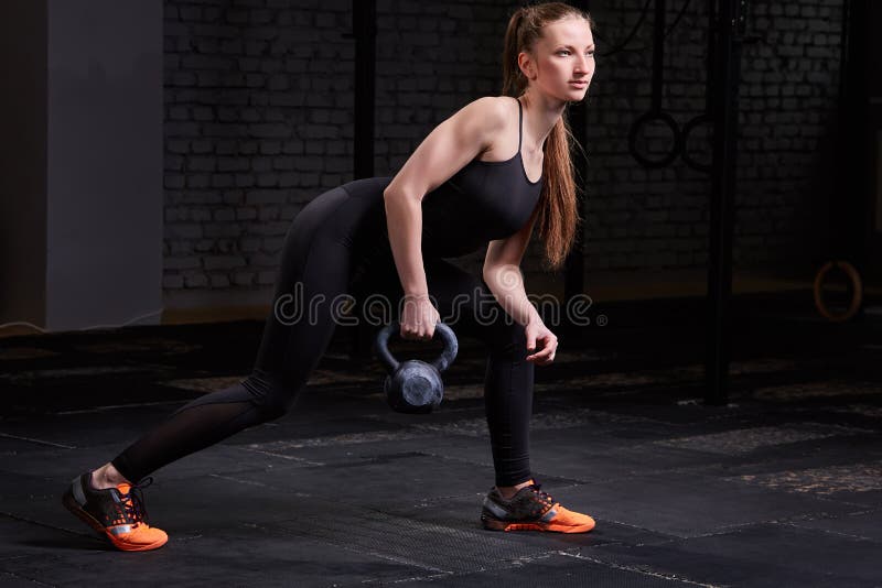 Giovane donna sportiva con l'ente muscolare che fa allenamento del crossfit con kettlebell su fondo scuro fotografie stock Giovane donna sportiva con l'ente muscolare che fa allenamento del crossfit con kettlebell su fondo scuro fotografie stock