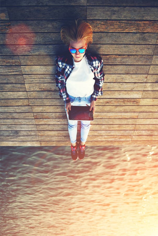 Giovane donna teenager che si rilassa sopra un molo di legno mentre prendendo autoritratto che sostiene compressa fotografia stock Giovane donna teenager che si rilassa sopra un molo di legno mentre prendendo autoritratto che sostiene compressa fotografia stock