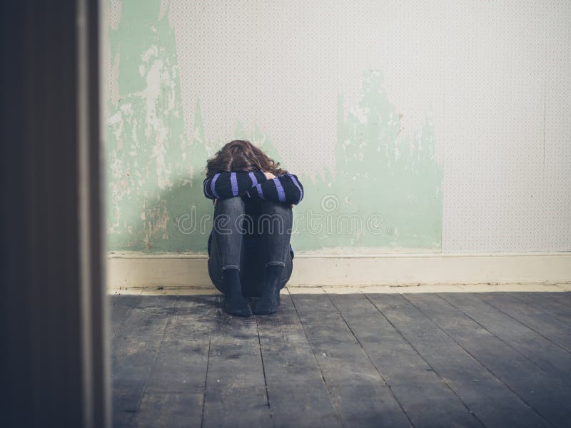 Giovane donna triste che si siede sul pavimento nella stanza vuota fotografia stock libera da diritti Giovane donna triste che si siede sul pavimento nella stanza vuota fotografia stock libera da diritti