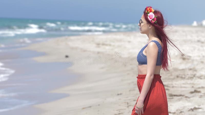 Giovane donna in una gonna rossa e cima blu con capelli rossi che volano nel vento ed in una corona floreale in suoi capelli cont