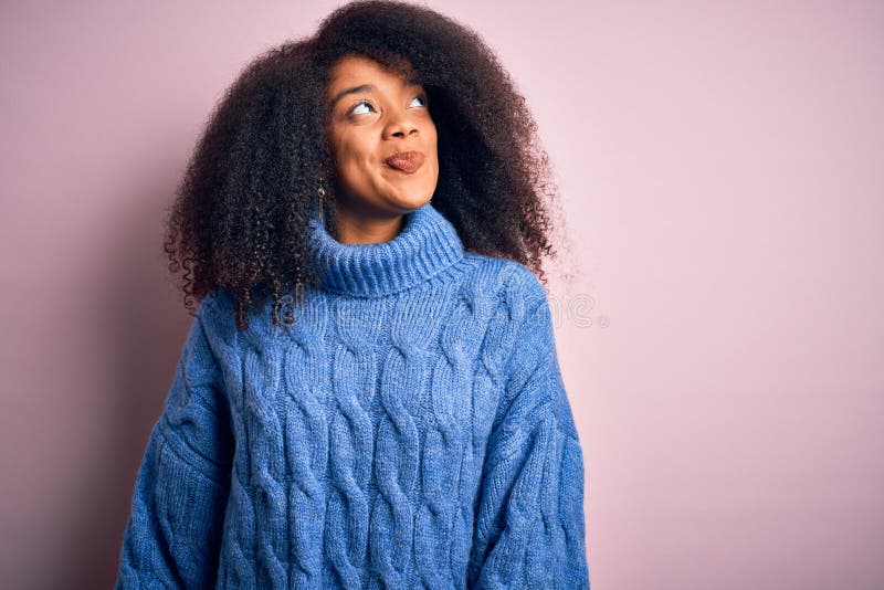 Giovane e bella donna afro-americana con capelli afro con maglione invernale su fondo rosa sorridendo guardando da un lato e immagini stock