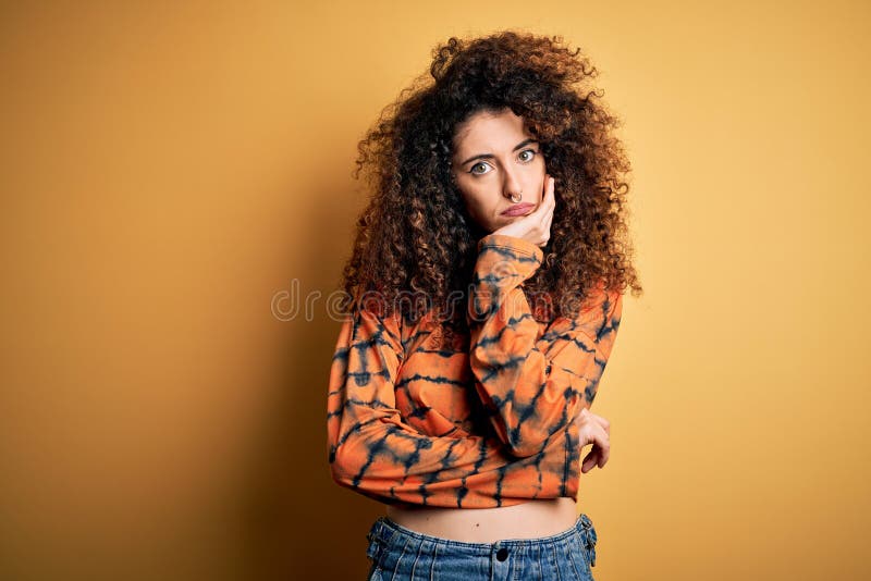 Giovane e bella donna brunetta con capelli ricci e piercing indossando una camicia informale che sembra stanca e annoiata fotografia stock libera da diritti