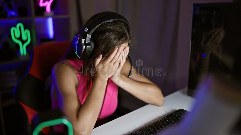 Giovane e squallida, giovane donna ispanica, smagliante, stressata da un flusso di videogame sovraccarico in una stanza di gioco s immagini stock libere da diritti