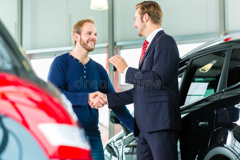 Giovane e venditore con l'auto nel concessionario auto fotografie stock Giovane e venditore con l'auto nel concessionario auto fotografie stock