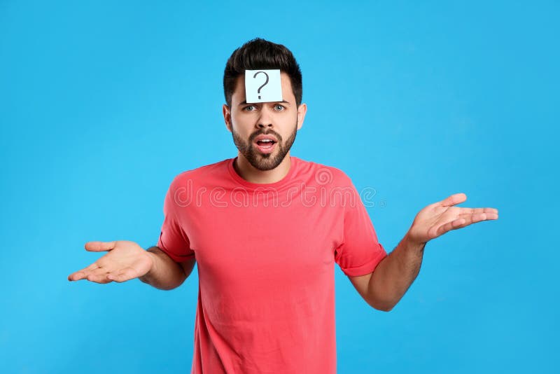 Emotional young man with question mark sticker on forehead against light blue background. Emotional young man with question mark sticker on forehead against light blue background