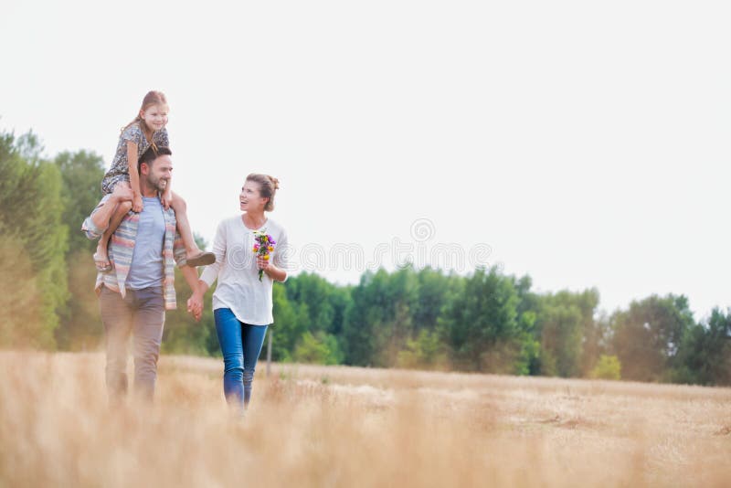 Photo of Young Caucasian family walking across field with young child on her fathers shoulders with the wife holding a bouquet of flowers. Photo of Young Caucasian family walking across field with young child on her fathers shoulders with the wife holding a bouquet of flowers
