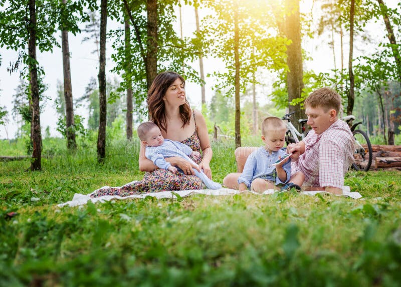 Giovane famiglia con due bambini piccoli su un picnic di estate nella p immagine stock libera da diritti Giovane famiglia con due bambini piccoli su un picnic di estate nella p immagine stock libera da diritti