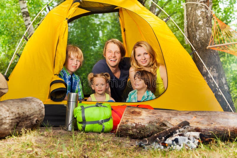 Portrait of happy young family, parents and three kids relaxing inside yellow tent on camping holiday in the woods. Portrait of happy young family, parents and three kids relaxing inside yellow tent on camping holiday in the woods