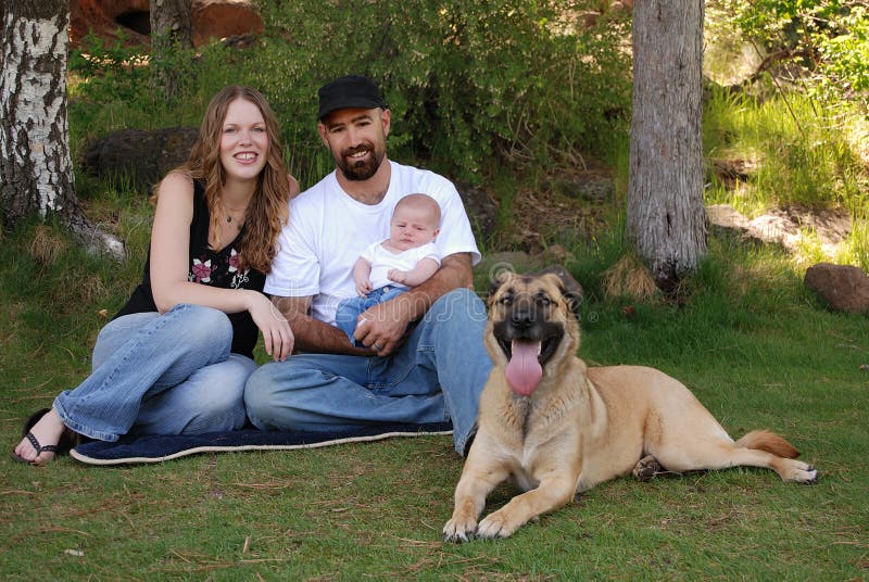 Giovane famiglia sorridente ed il loro cane nella sosta fotografia stock libera da diritti Giovane famiglia sorridente ed il loro cane nella sosta fotografia stock libera da diritti
