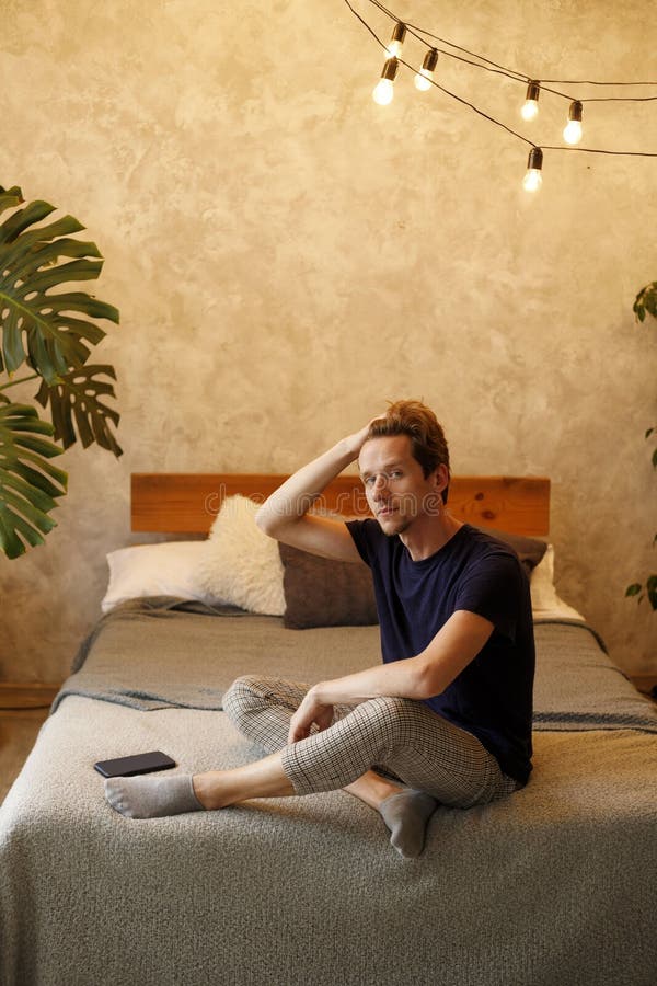 Giovane felice seduto a letto dopo essersi svegliato e aver dato il benvenuto al mattino tenendo la testa immagini stock