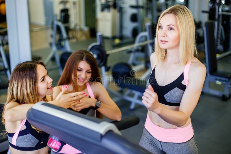 Giovane funzionamento biondo sulla pedana mobile alla palestra Un sorriso di due donne di forma fisica la motiva fotografia stock Giovane funzionamento biondo sulla pedana mobile alla palestra Un sorriso di due donne di forma fisica la motiva fotografia stock