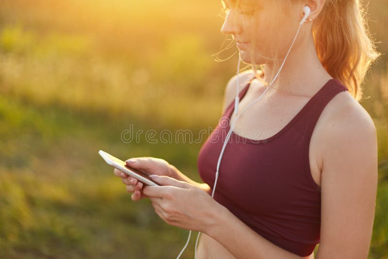 Giovane funzionamento sportivo della donna, facendo sport, cima d'uso, ascoltando la musica con le cuffie ed il telefono cellular immagine stock Giovane funzionamento sportivo della donna, facendo sport, cima d'uso, ascoltando la musica con le cuffie ed il telefono cellular immagine stock
