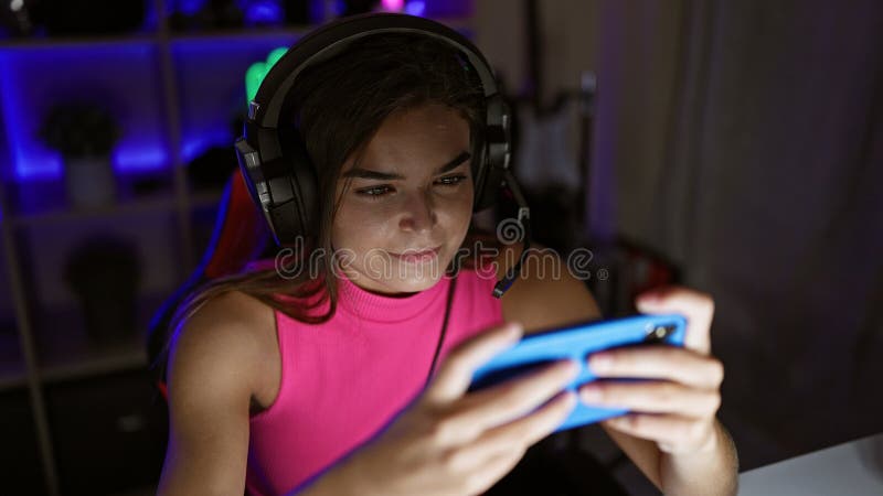 Giovane giocatore ispanica sicura di sé, ritratto di una bellissima smagliatrice che gioca un videogioco sul suo smartphone all'in immagine stock libera da diritti