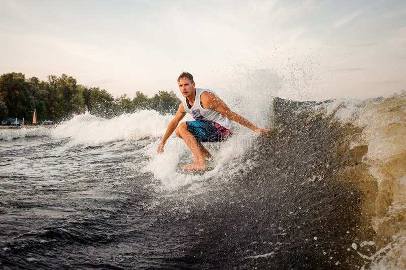 Giovane guida attiva dell'uomo sul wakeboard sull'aria aperta fotografia stock libera da diritti Giovane guida attiva dell'uomo sul wakeboard sull'aria aperta fotografia stock libera da diritti