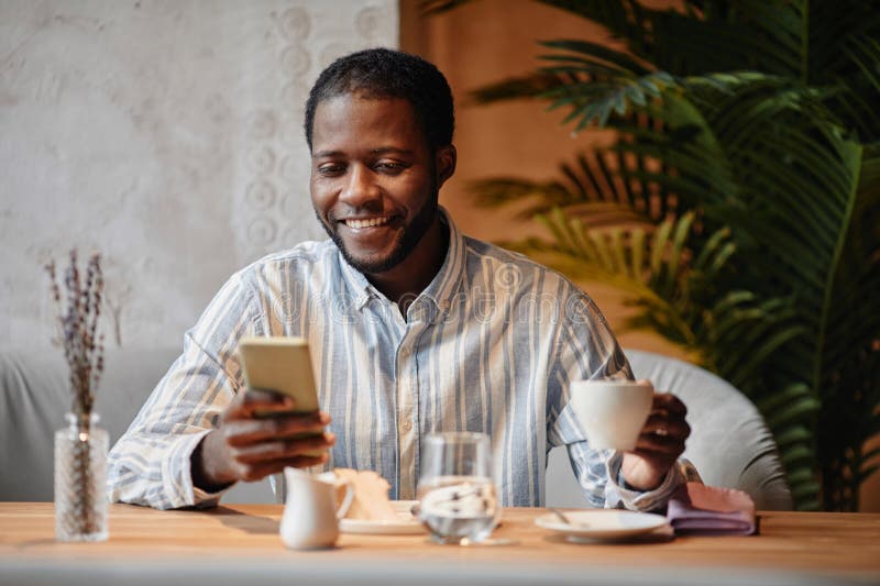 Giovane imprenditore americano africano guarda con sorriso lo schermo degli smartphone fotografie stock