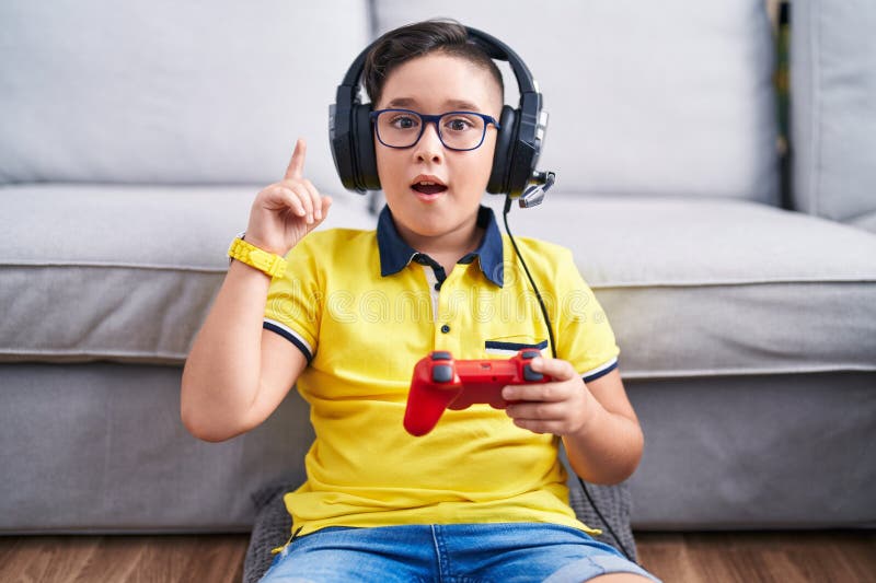 Giovane ispanico che gioca a videogioco con controller che indossa cuffie che punta il dito contro un'idea di successo fotografie stock libere da diritti