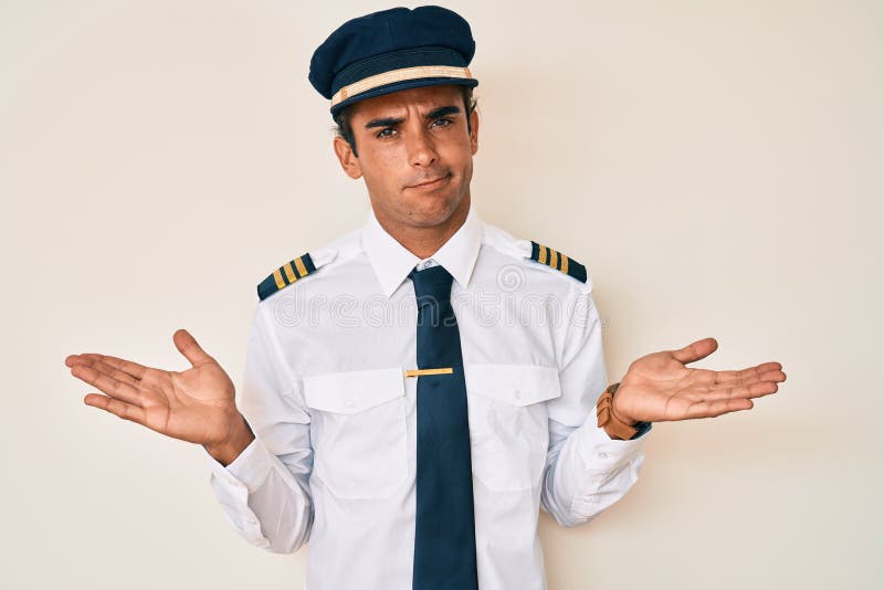 Young hispanic man wearing airplane pilot uniform clueless and confused with open arms, no idea concept. Young hispanic man wearing airplane pilot uniform clueless and confused with open arms, no idea concept