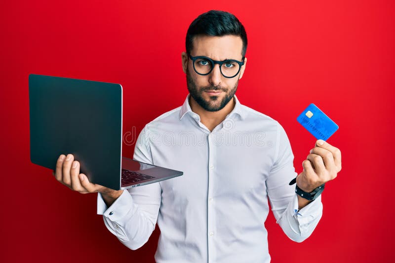 Young hispanic man wearing business style holding laptop and credit card skeptic and nervous, frowning upset because of problem. negative person. Young hispanic man wearing business style holding laptop and credit card skeptic and nervous, frowning upset because of problem. negative person