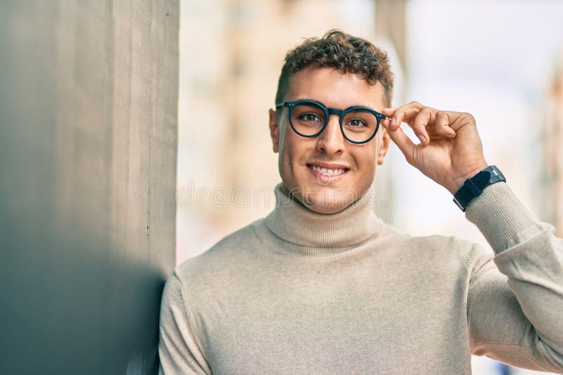Giovane ispanico sorridente felice indossando degli occhiali in città