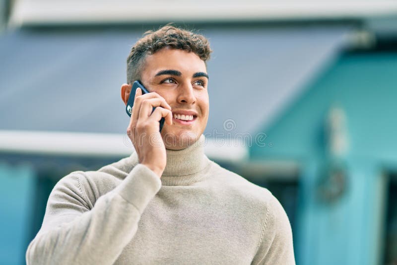 Giovane ispanico sorridente felice mentre parla allo smartphone della città fotografia stock
