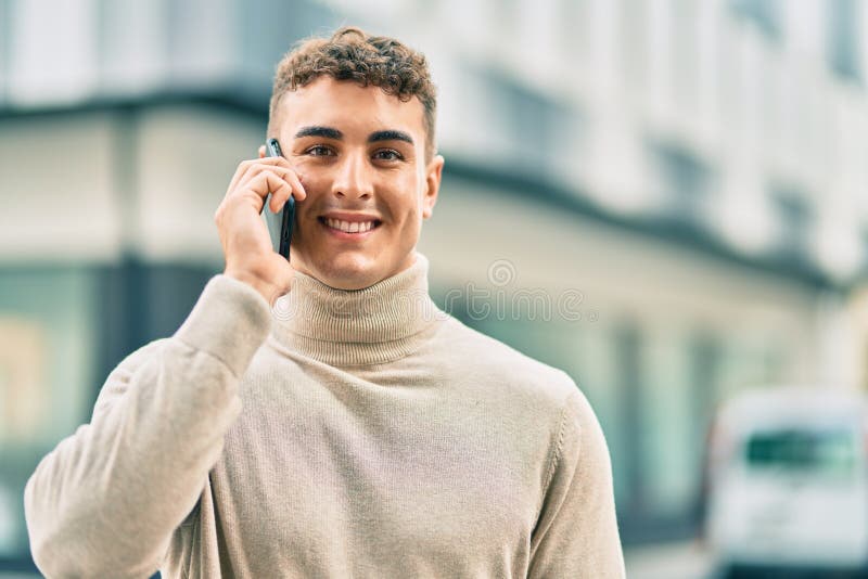 Giovane ispanico sorridente felice mentre parla allo smartphone della città immagine stock